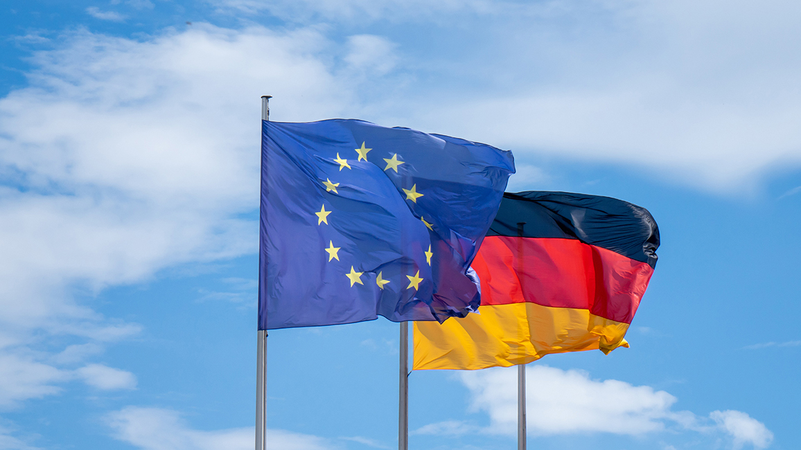 Eine EU-Flagge und eine Deutschland-Flagge flattern im Wind.