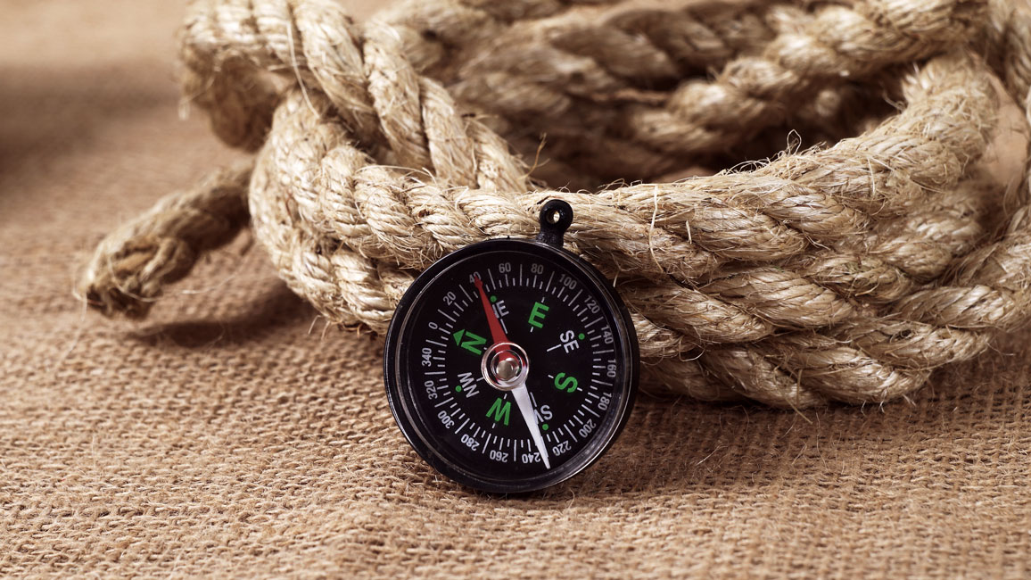 A compass leaning against a rolled-up rope.