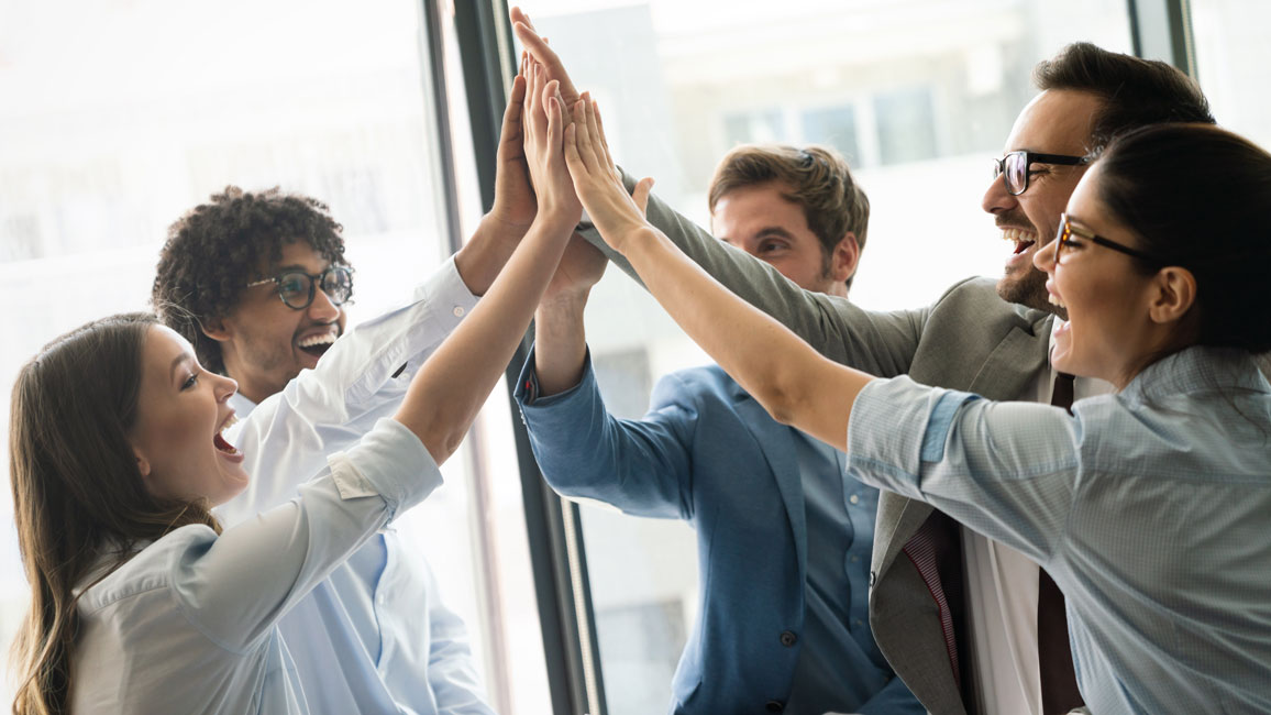 Eine Gruppe junger Männer und Frauen in einem Bürogebäude schlägt ihre Hände zu einem "High Five" zusammen.